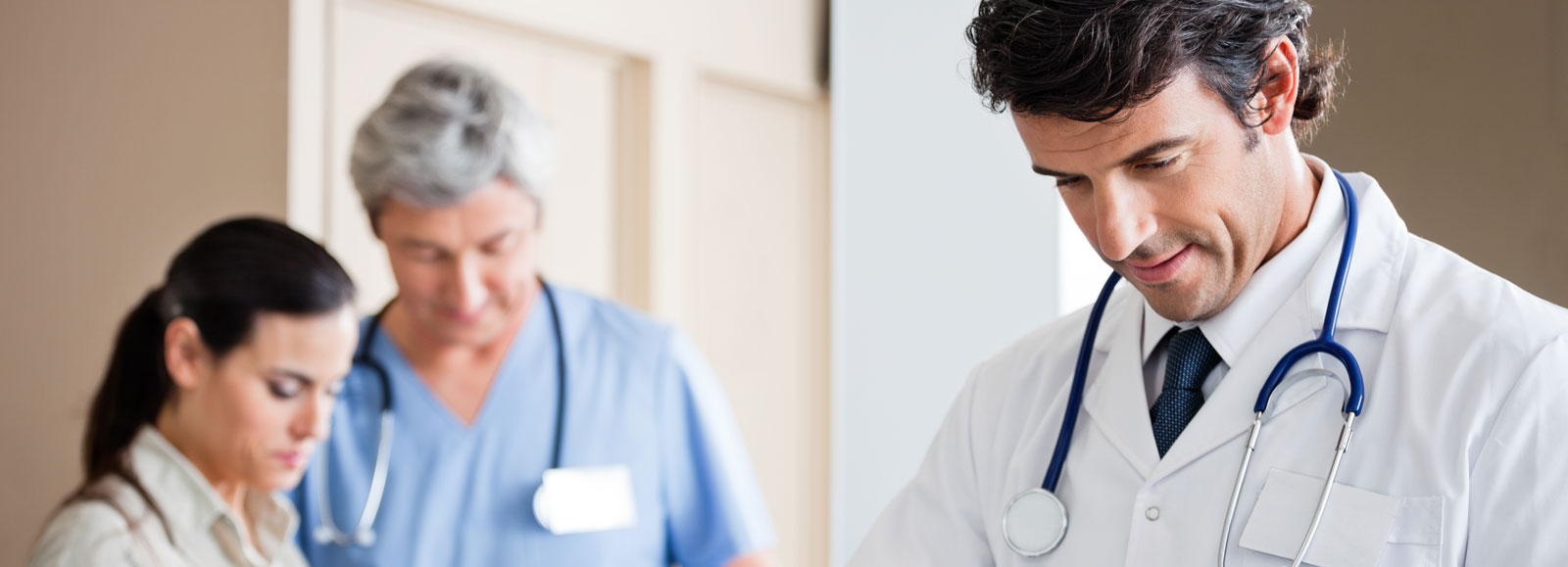 Physician in a white coat with a stethoscope, medical staff in the background
