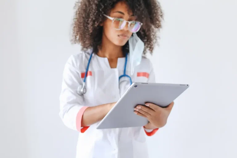 Physician in a white coat reviewing notes on a tablet